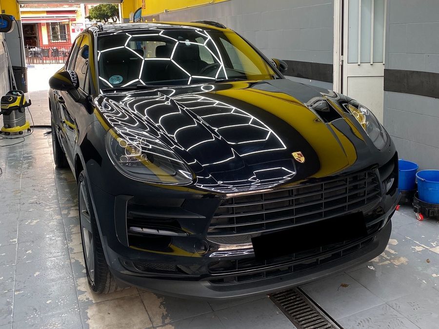 Porsche Macan negro en el estudio con el techo hexagonal reflejado en el capó