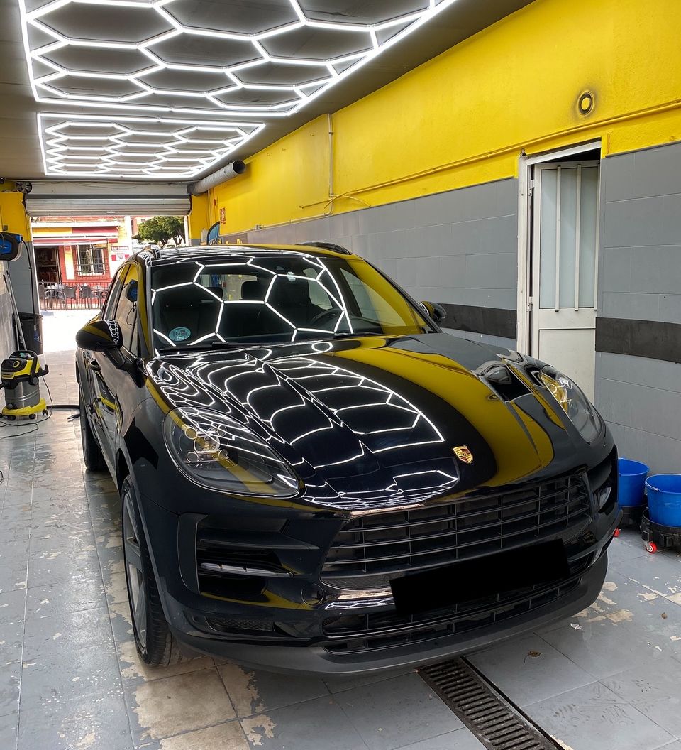Porsche Macan negro en nuestro lavadero de coches de San Pedro de Alcántara, con el techo de luz LED hexagonal reflejado en el capó